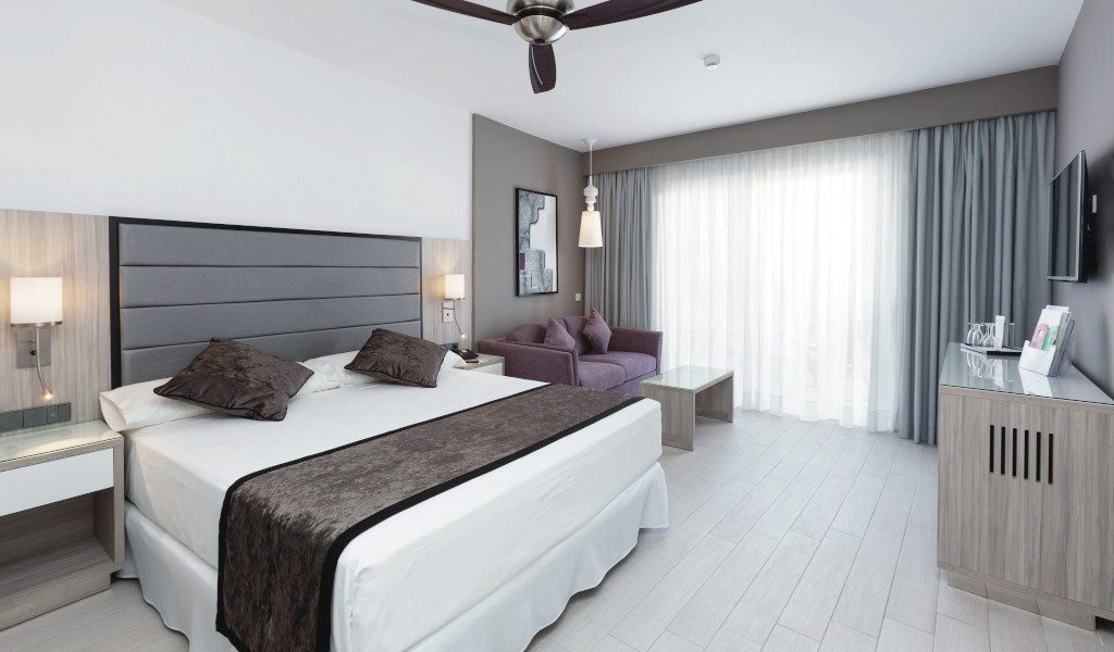 Chambre d'hôtel moderne à Tenerife avec lit, canapé et grande fenêtre.
