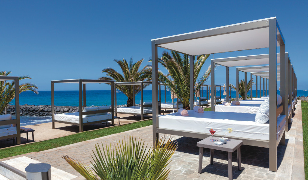 Lit baldaquin face à la mer à Tenerife avec palmiers et océan en arrière-plan.