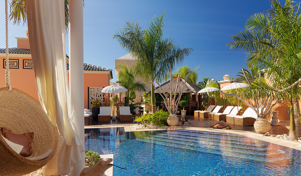 Piscine entourée de transats et palmiers dans une villa à Tenerife.