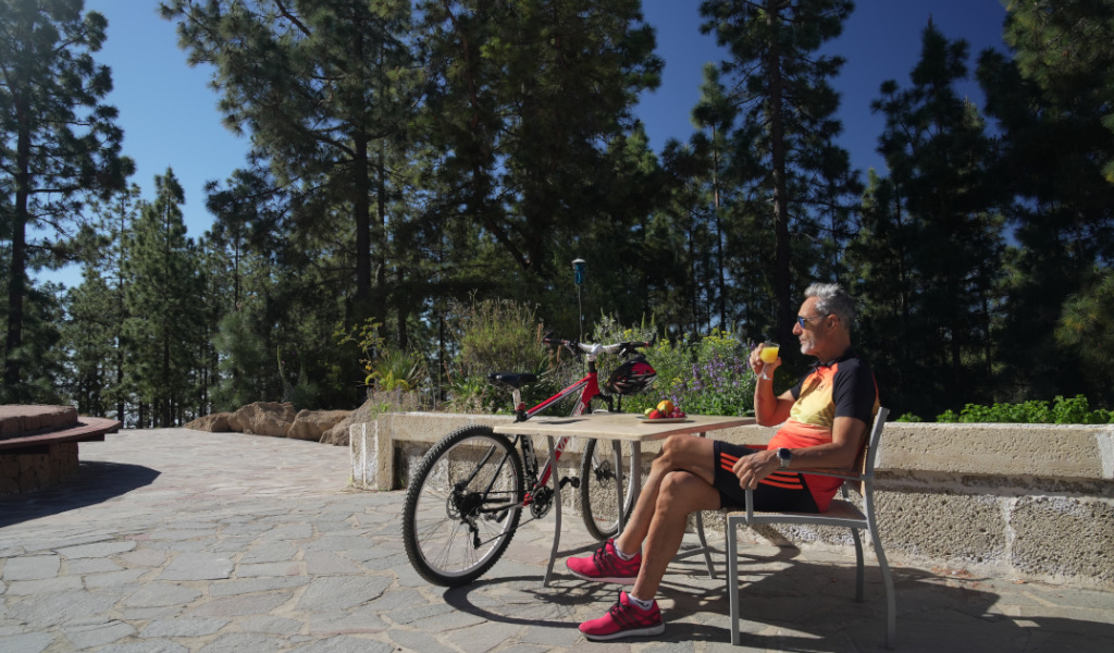 Un homme boit un jus à une table en plein air à La Orotava, Tenerife, avec un vélo à côté.