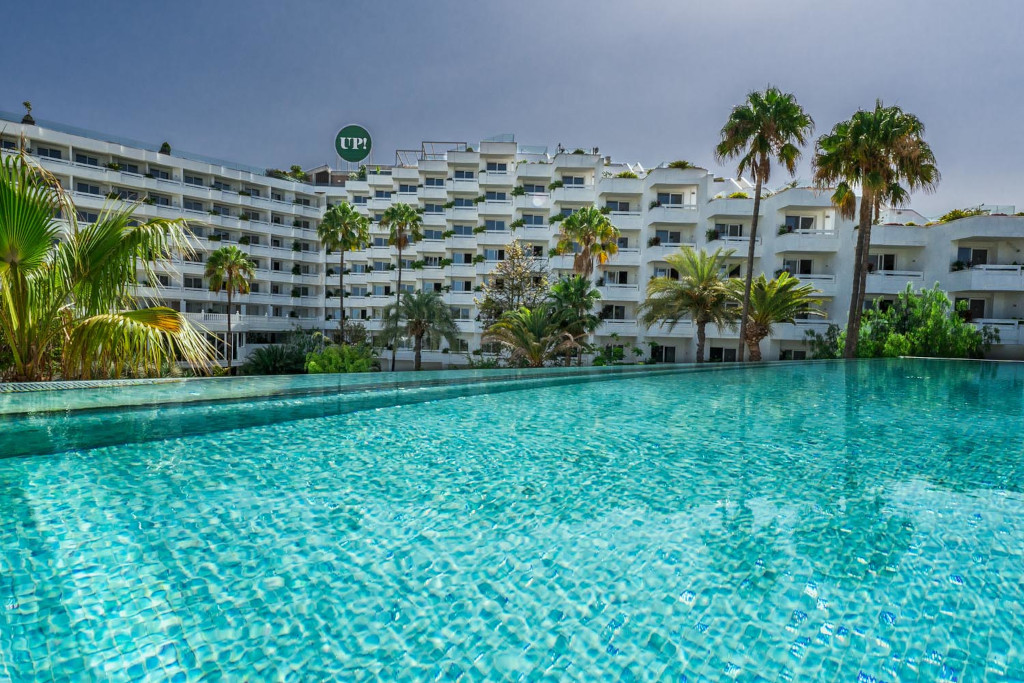 Piscine à débordement donnant sur un hôtel à Tenerife avec palmiers.