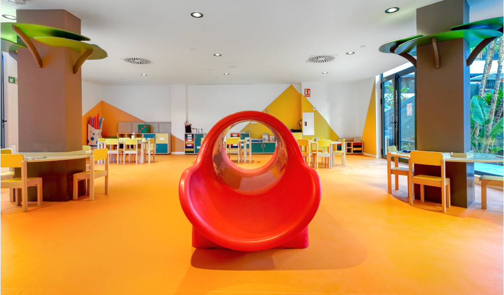 Salle de jeux pour enfants avec tables, chaises et toboggan rouge à Tenerife.