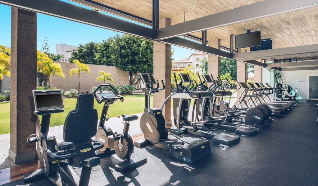 Salle de sport avec vélos et tapis de course à Tenerife, vue sur jardin extérieur.