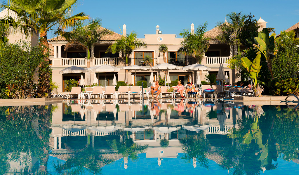 Hôtel à Tenerife avec piscine, palmiers et chaises longues sous le soleil.