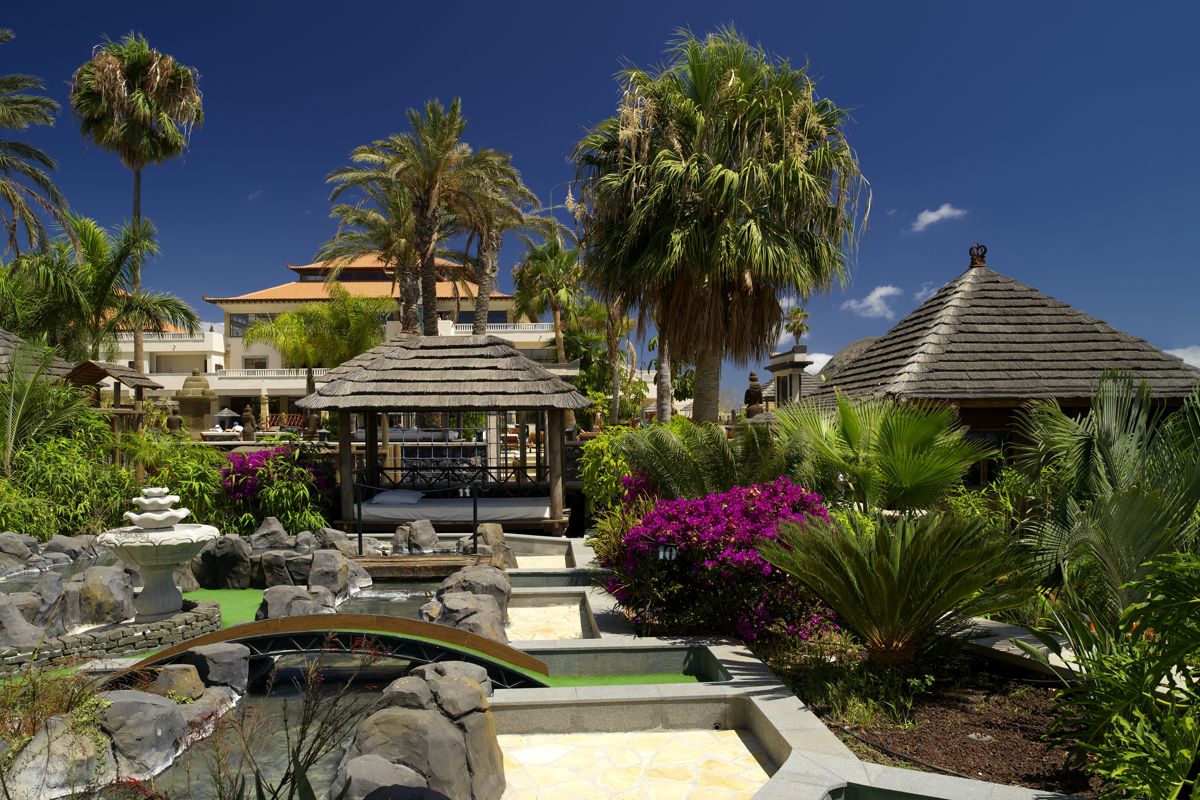 Jardin tropical à Tenerife avec palmiers, fleurs et pavillons en bois.