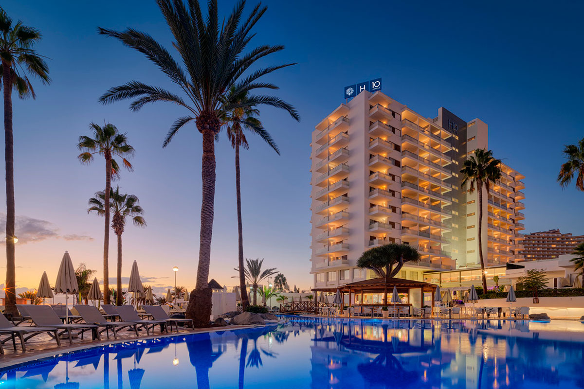 Hôtel avec piscine au coucher du soleil à Tenerife, entouré de palmiers.