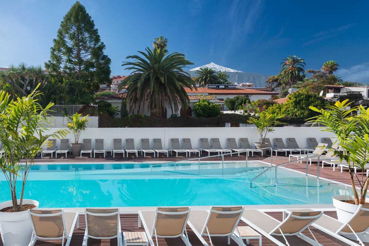 Piscine avec chaises longues, palmiers et vue sur le mont Teide à Tenerife.