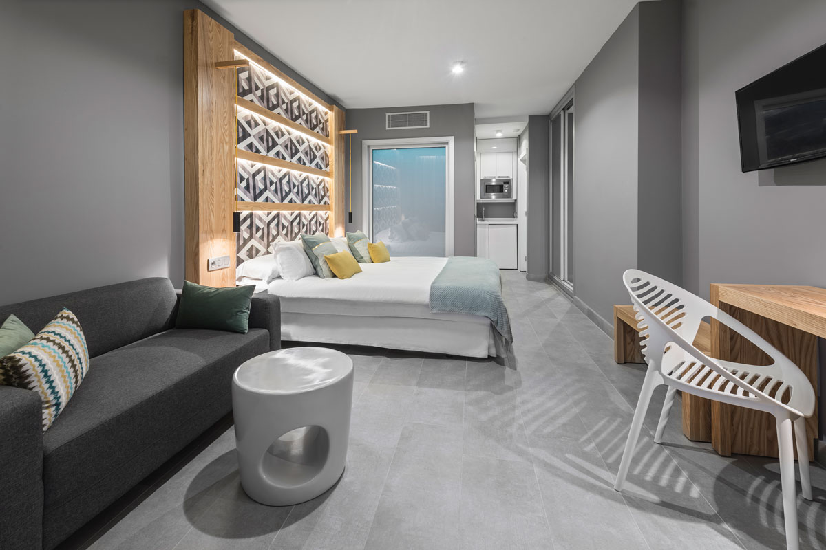 Chambre d'hôtel moderne à Tenerife avec lit, canapé, table et kitchenette.