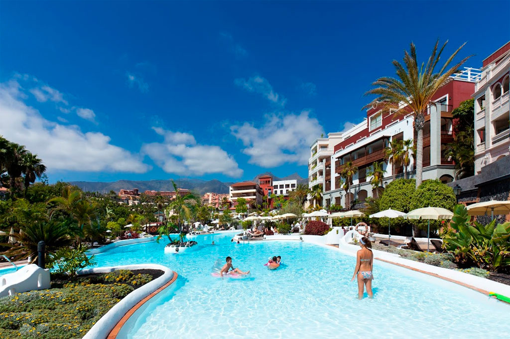Piscine d'un hôtel à Tenerife entourée de bâtiments et palmiers sous ciel bleu.