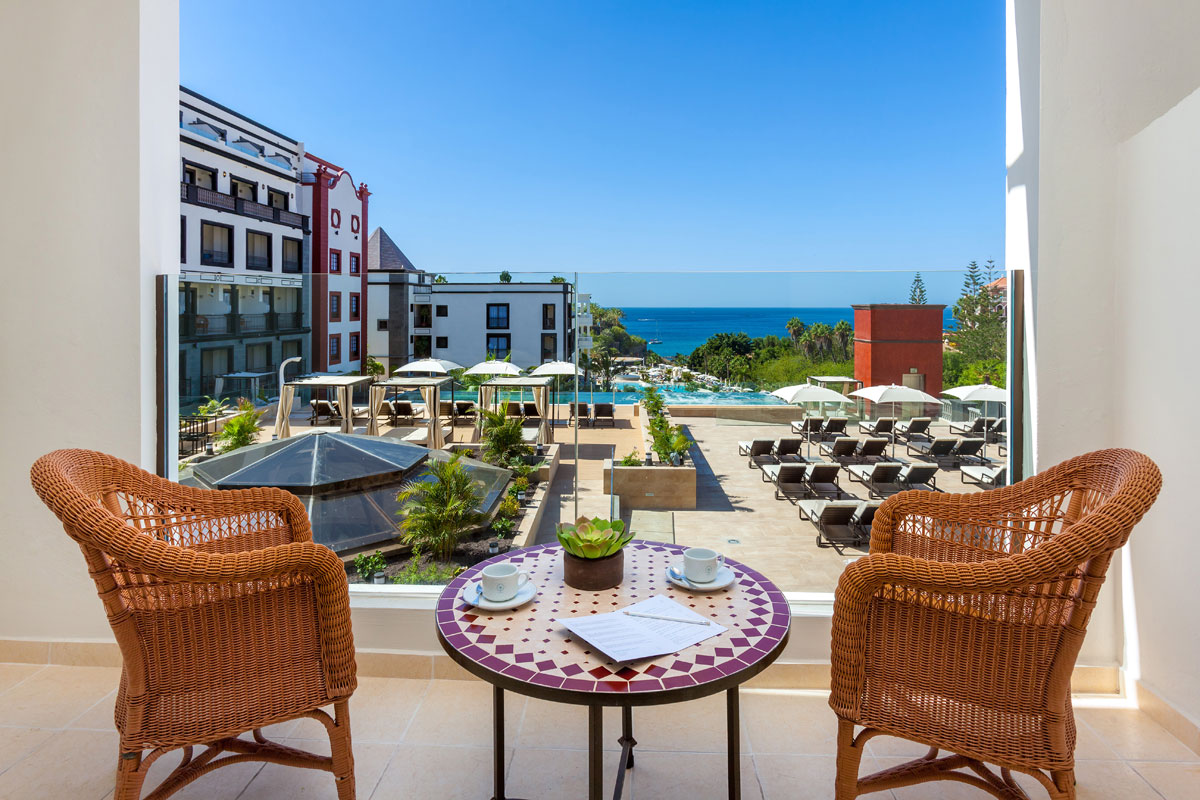 Balcon avec vue sur l'océan et la piscine à Tenerife, deux tasses de café sur une table.