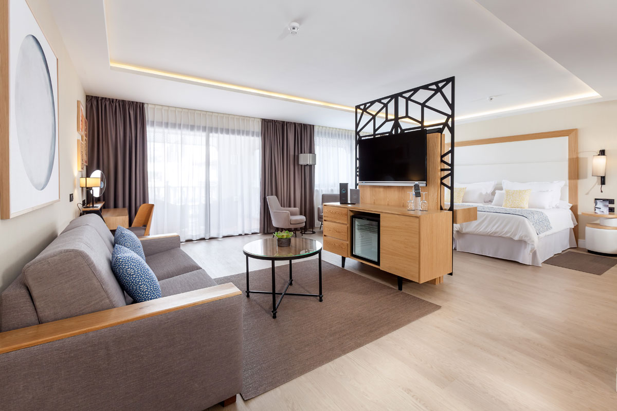 Salon moderne avec canapé, table basse, télé, et lit dans un hôtel à Tenerife.