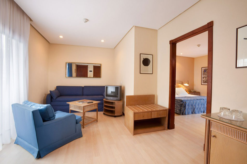 Salon avec canapé bleu et télé, chambre au fond à Tenerife.