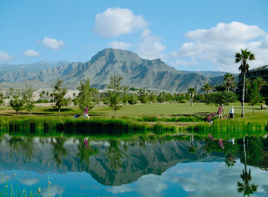 Golfeurs marchant près d'un étang, montagnes en arrière-plan à Tenerife.