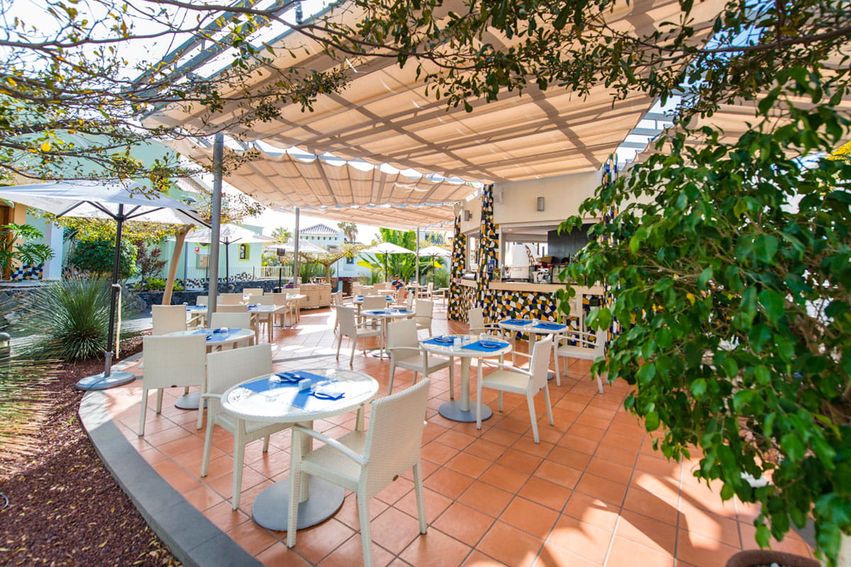 Terrasse extérieure d'un café à Tenerife avec tables et chaises sous un auvent.