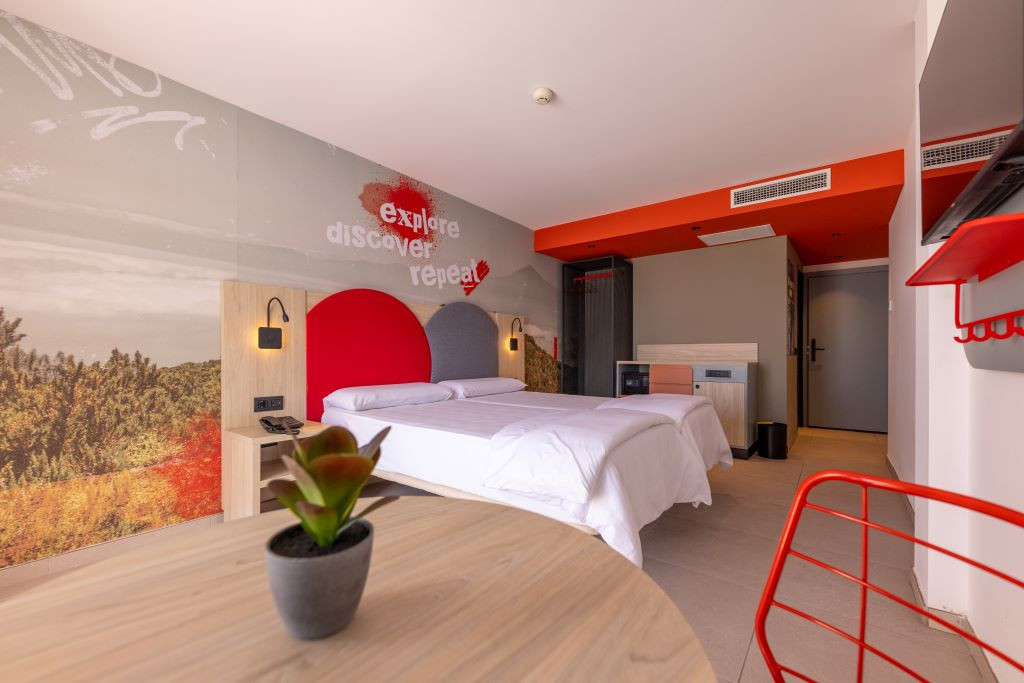 Chambre moderne avec lit double, plan d’étage et fresque qui indique explorer, découvrir, répéter.