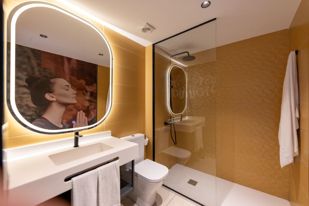 Salle de bain avec douche, lavabo, miroir illuminé et photographie d’une femme méditant à Tenerife.
