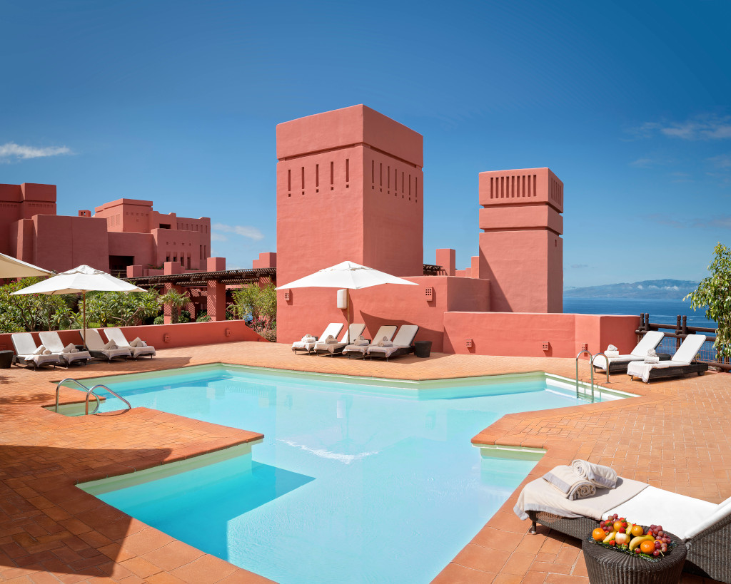 Piscine extérieure avec transats et parasols, complexe rouge en arrière-plan à Tenerife.