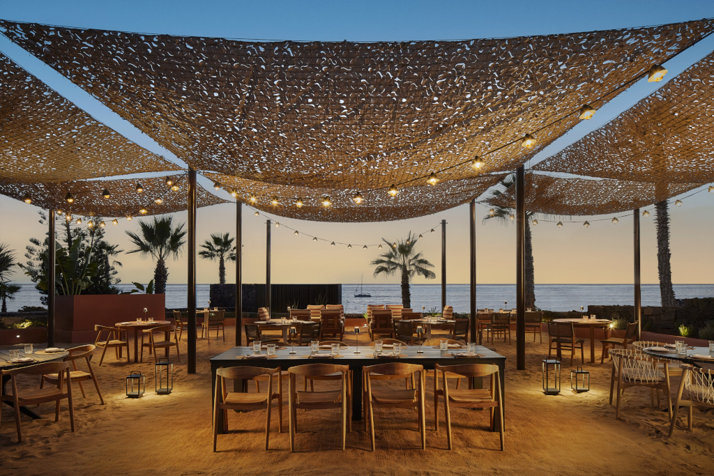 Terrasse de restaurant au coucher du soleil à Tenerife, vue sur l'océan et palmiers.
