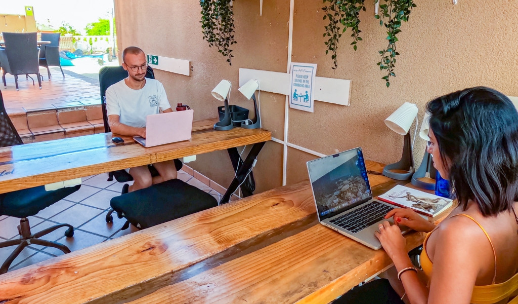 Deux personnes travaillent sur des ordinateurs portables à Tenerife, espace intérieur avec tables en bois.