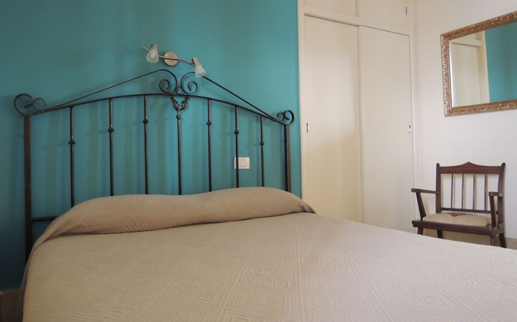 Lit avec tête de lit en métal, mur turquoise et armoire dans une chambre à Tenerife.