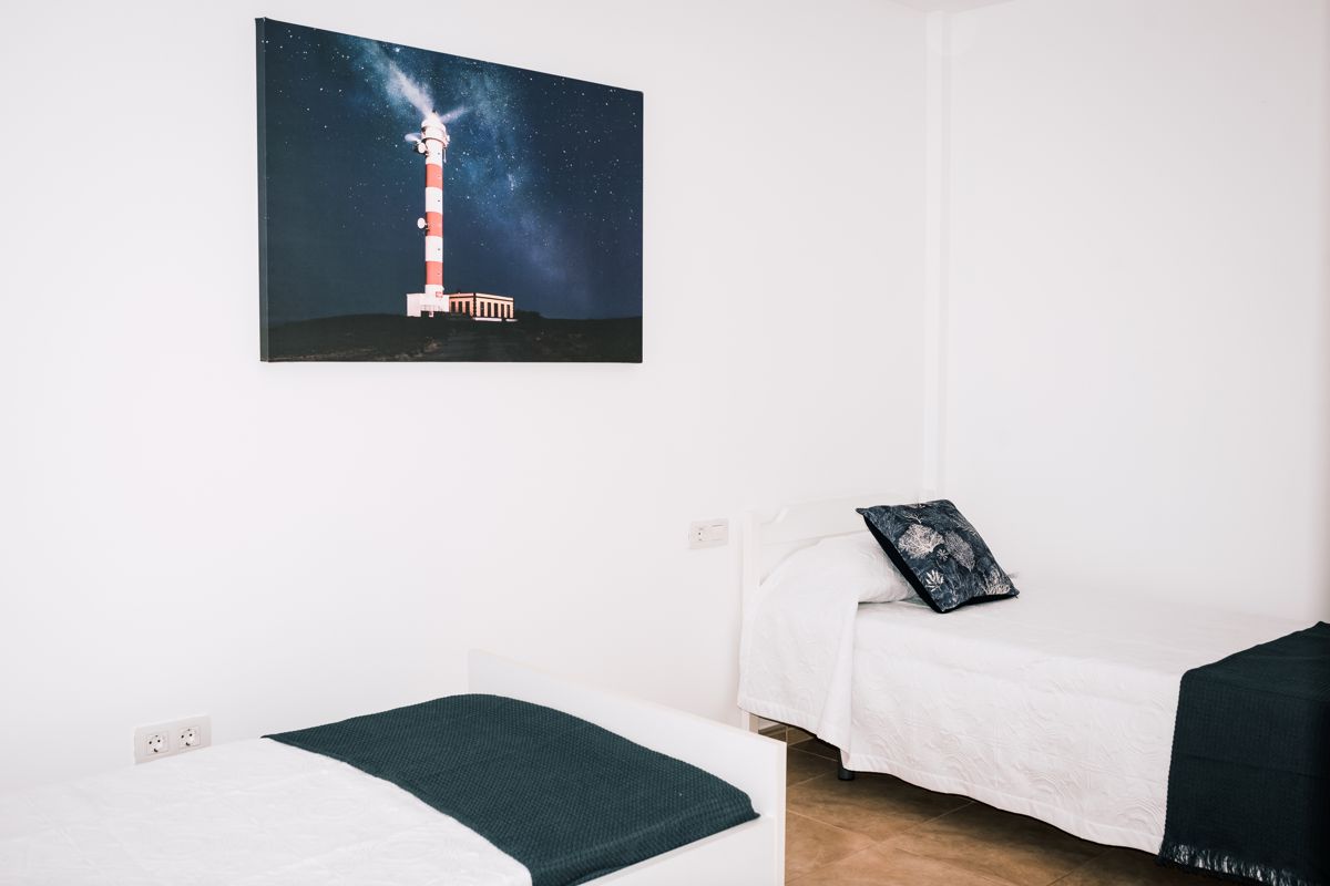 Deux lits avec tableau du phare dans une chambre à Tenerife.