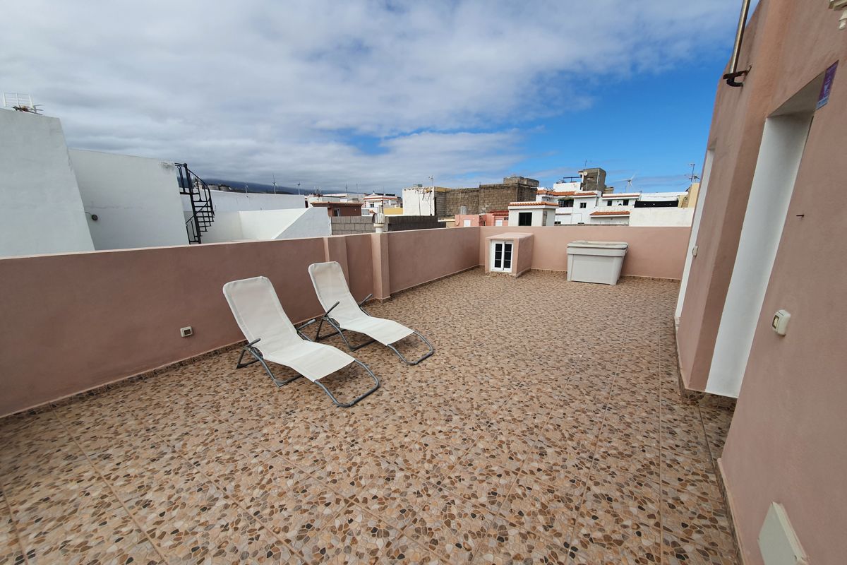 Deux chaises longues sur une terrasse à Tenerife, vue sur bâtiments voisins.