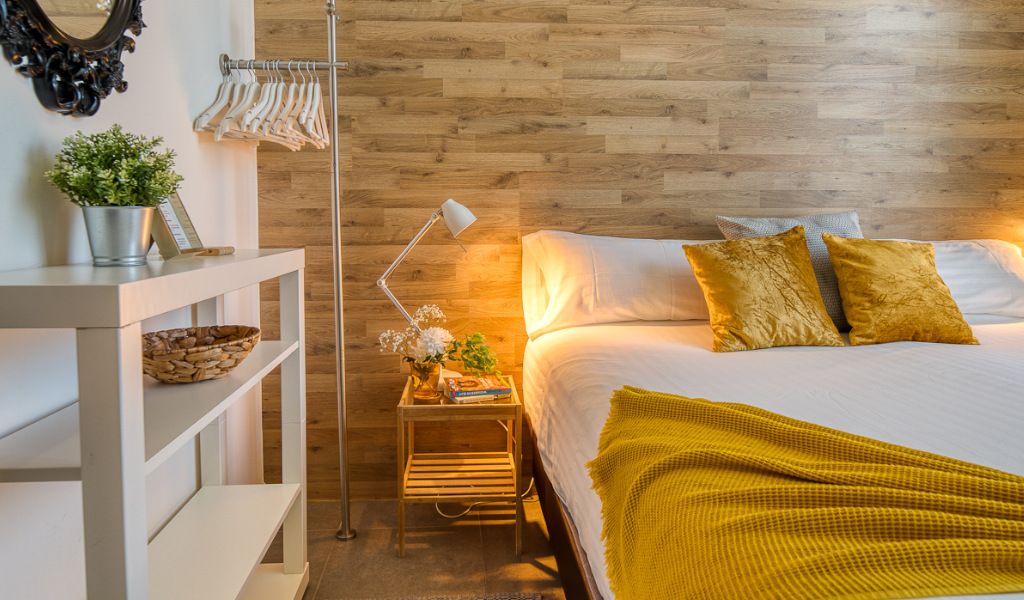 Lit avec coussins jaunes et plaid, étagère avec plantes et cintres dans une chambre de Tenerife.