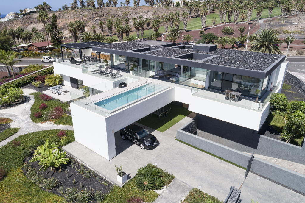 Villa moderne avec piscine à Tenerife, entourée de jardins et route adjacente.