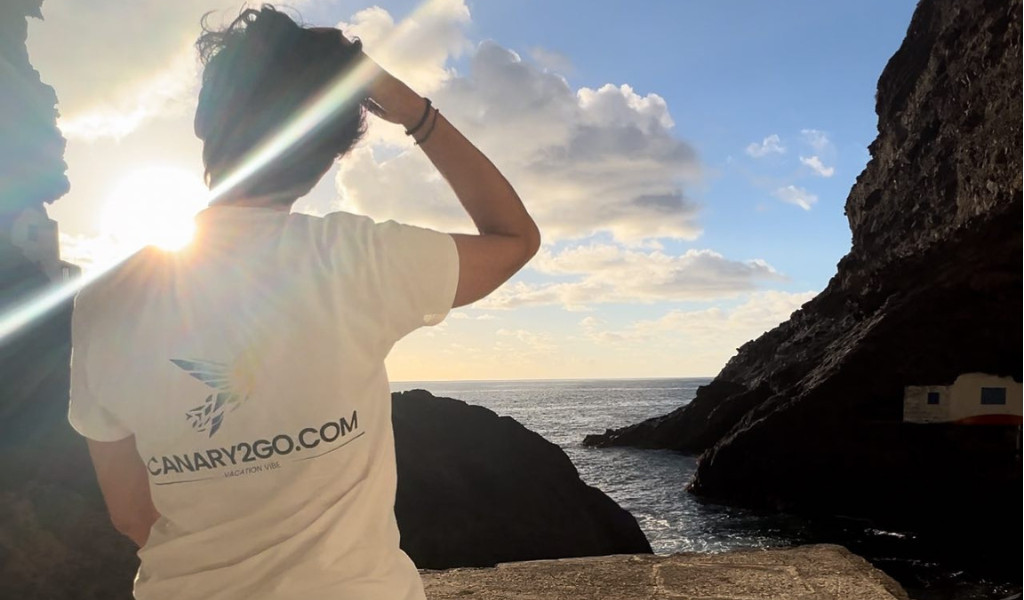 Personne en T-shirt blanc avec texte CANARY2GO.COM regardant la mer à Tenerife.