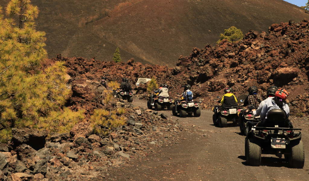Personnes en quad sur un chemin volcanique à Tenerife entouré de roches et de végétation.