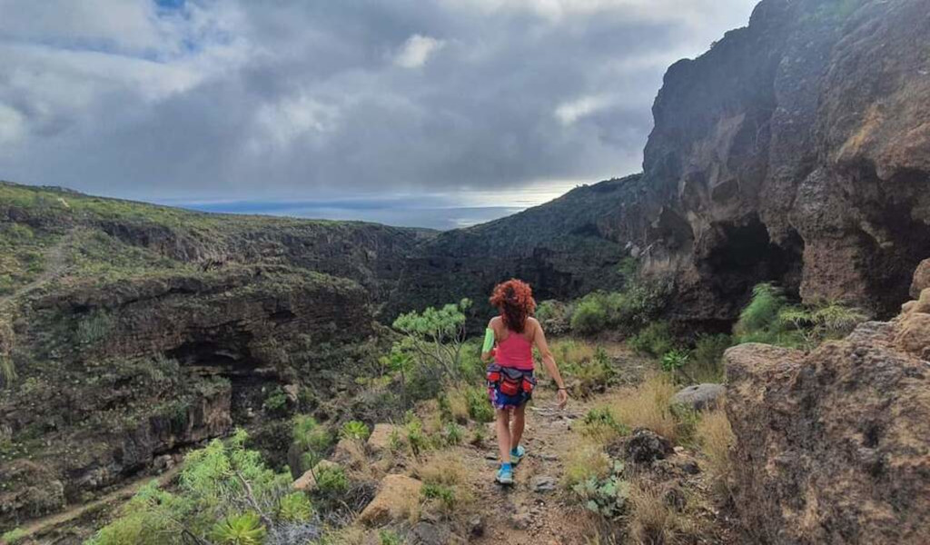 Femme marchant sur sentier de randonnée à Tenerife, montagnes et océan en arrière-plan.
