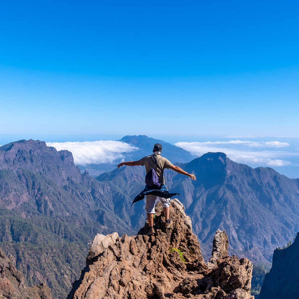 Un randonneur debout sur un sommet rocheux à Tenerife, vue sur les montagnes et les nuages.