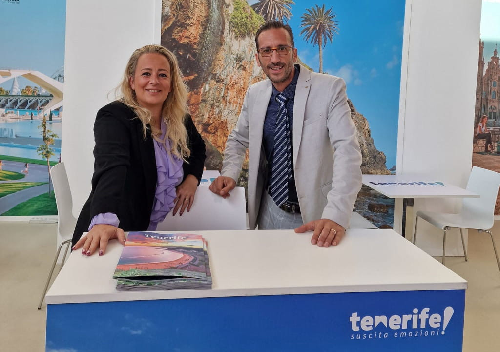Deux personnes souriant à un stand promotionnel de Tenerife avec des brochures sur la table.