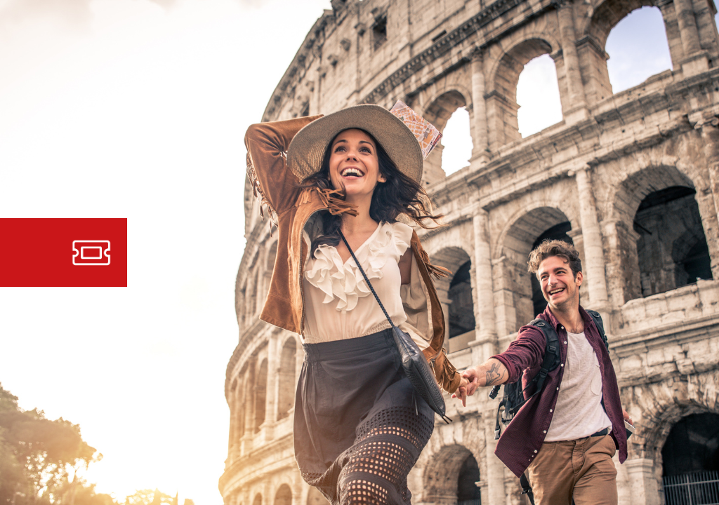 Couple de touristes souriants courant devant le Colisée de Rome au coucher du soleil, avec sacs à dos et vêtements décontractés.