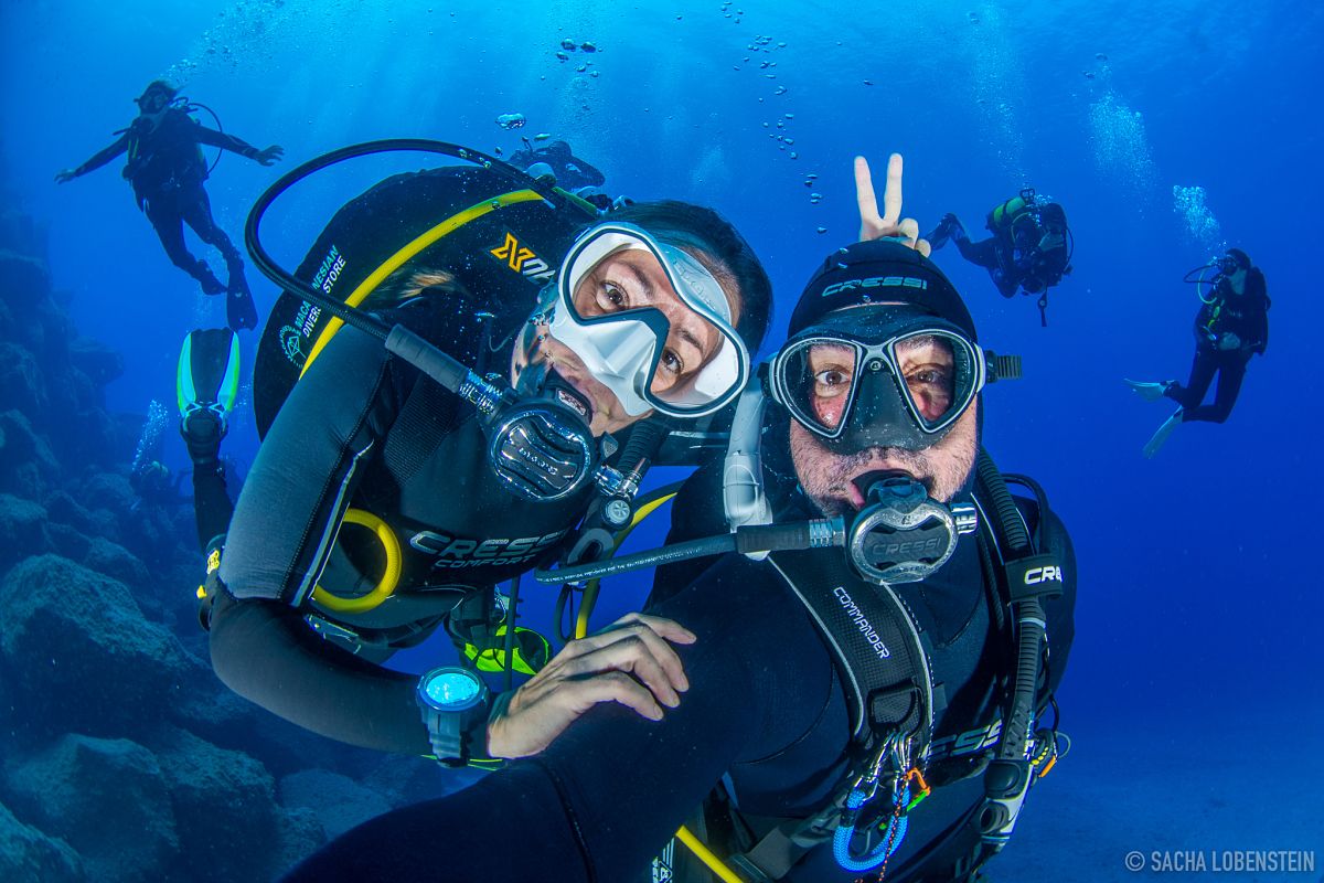 Des plongeurs souriant sous l’eau à Tenerife, accompagnés d’autres en arrière-plan.