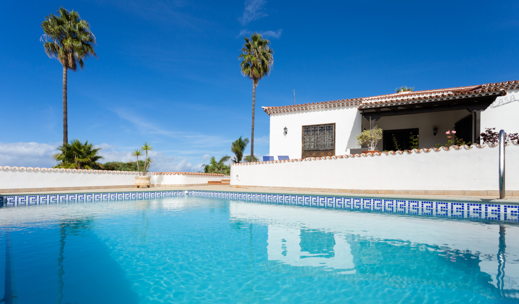 Piscine et maison avec palmiers à Tenerife sous un ciel bleu.