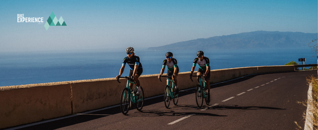 Cyclistes sur la route avec l’océan et la vue sur Tenerife. Texte : Expérience à vélo.