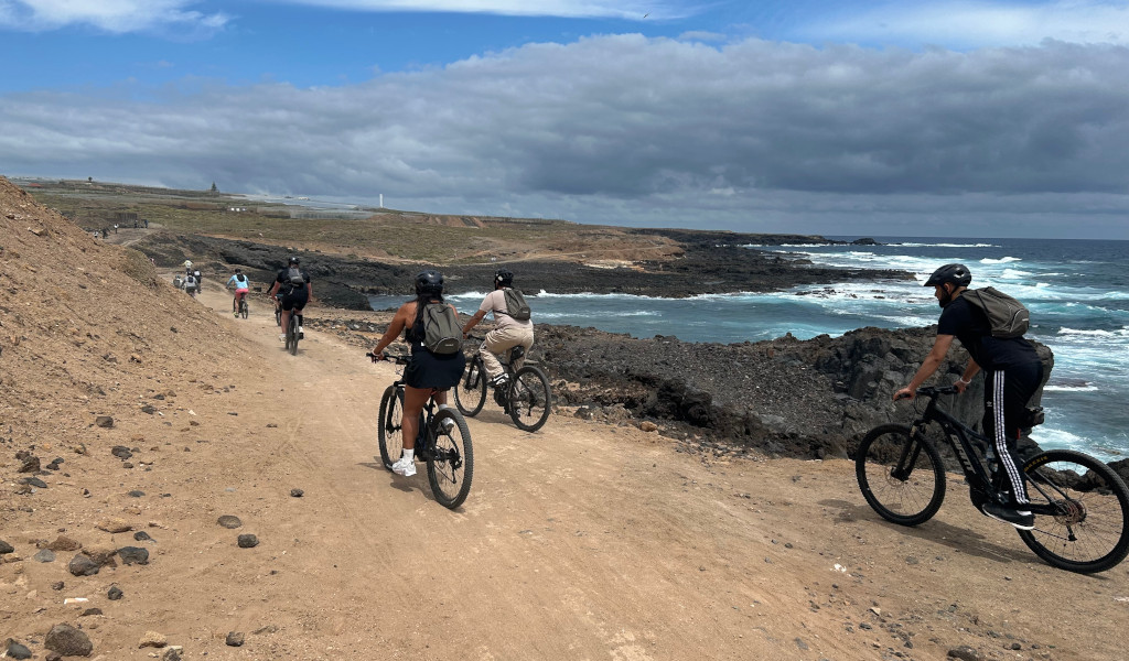 Des cyclistes roulant le long d’un sentier côtier à Tenerife, au bord de la mer et sous un ciel nuageux.