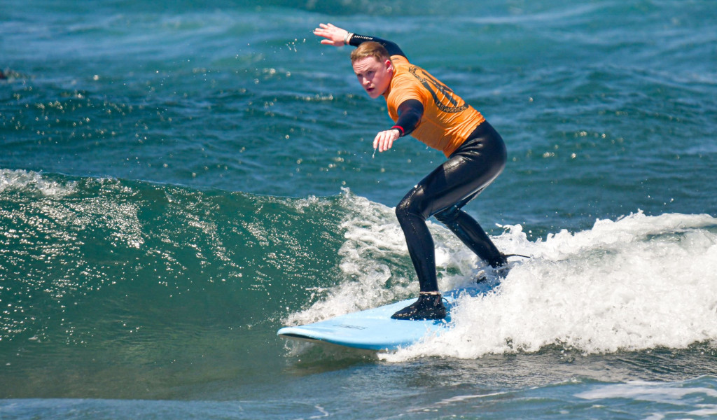 Personne surfant une vague à Tenerife, vêtue d’une combinaison de plongée orange.