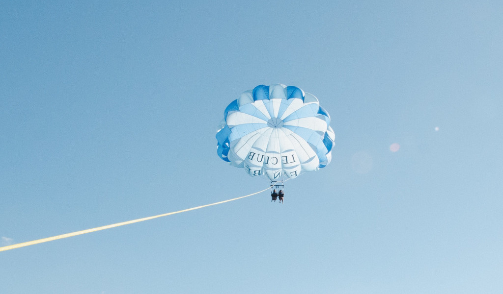 Parachute ascensionnel au-dessus du ciel de Tenerife avec des gens sous des parachutes blancs et bleus.