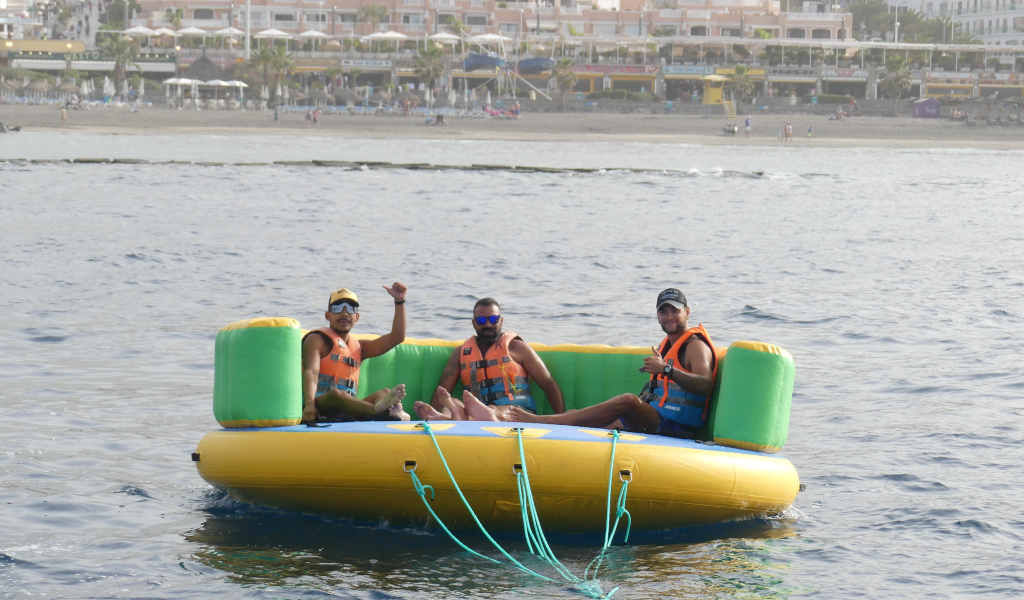 Trois personnes sur une plateforme gonflable en mer, Playa de las Americas en arrière-plan, Tenerife.