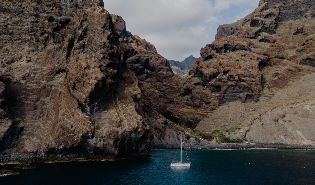 Voilier sur la côte rocheuse de Tenerife avec des eaux bleues et des montagnes en arrière-plan.