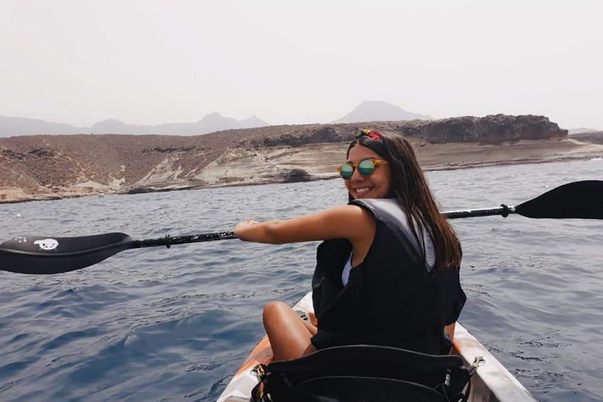 Une personne pagayant en kayak dans les eaux de Tenerife, avec un paysage montagneux en arrière-plan.