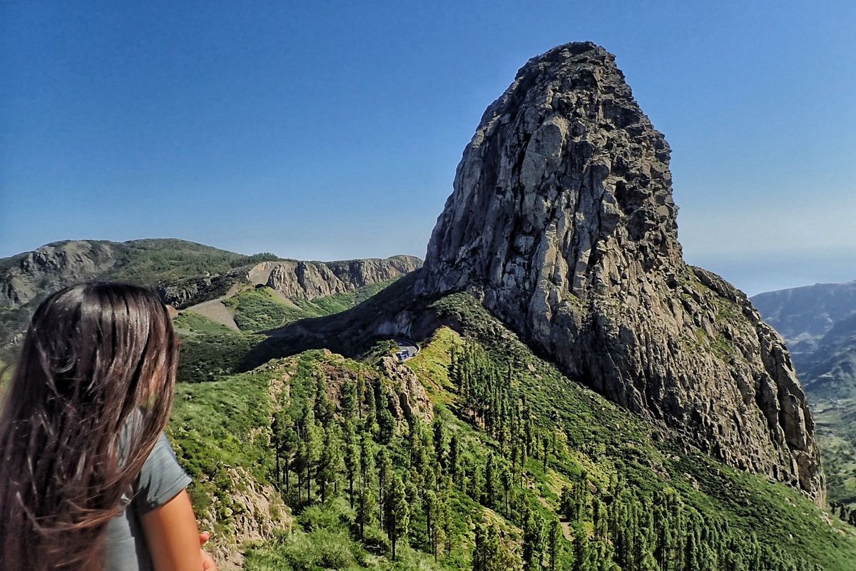 Femme observant le Roque de Agando à Tenerife, entourée de végétation.