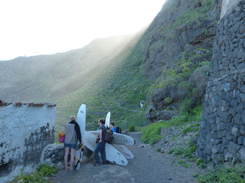 Des gens avec des planches de surf marchant le long d’un sentier à Tenerife, entourés de montagnes.