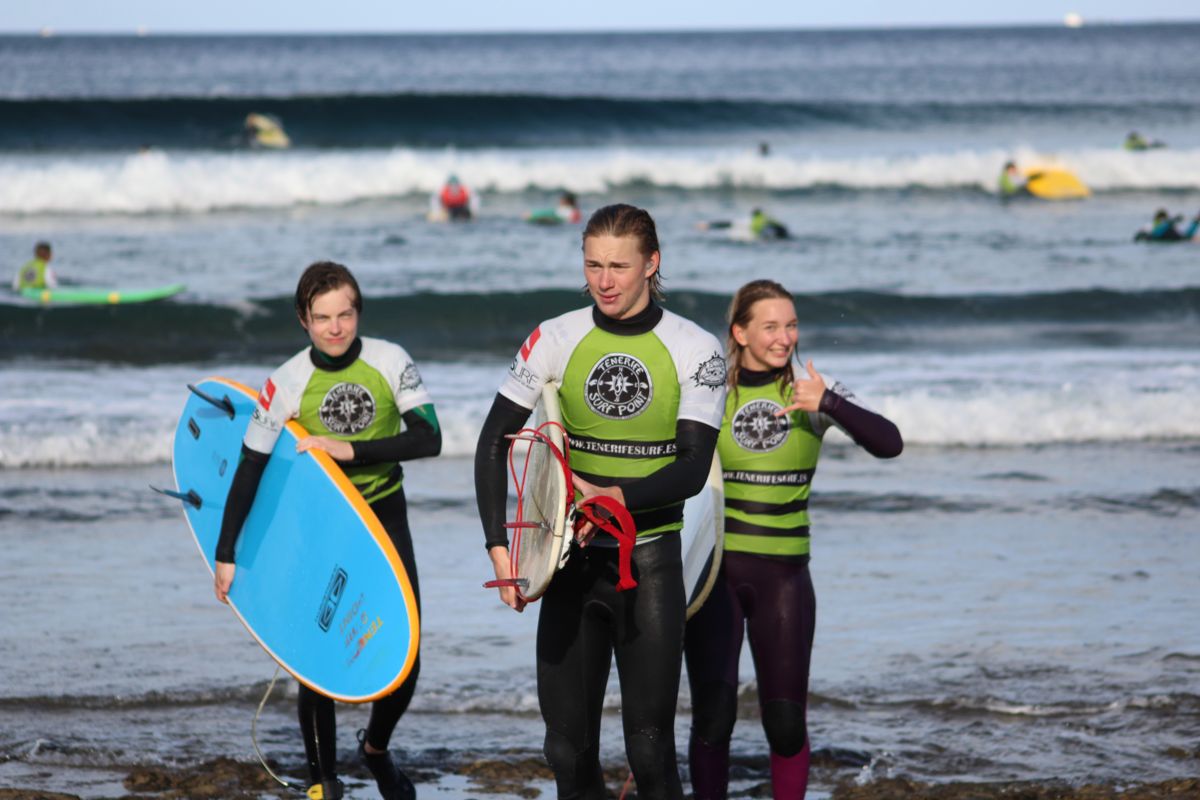 Des surfeurs sur la plage de Tenerife, avec des planches et des combinaisons, près de la mer.