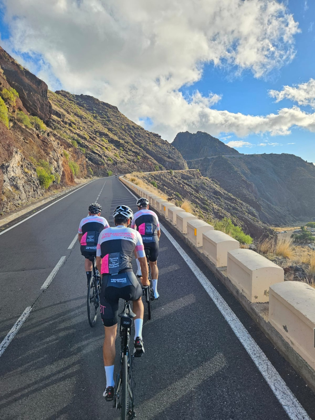 Des cyclistes gravissant une route montagneuse à Tenerife sous un ciel partiellement nuageux.