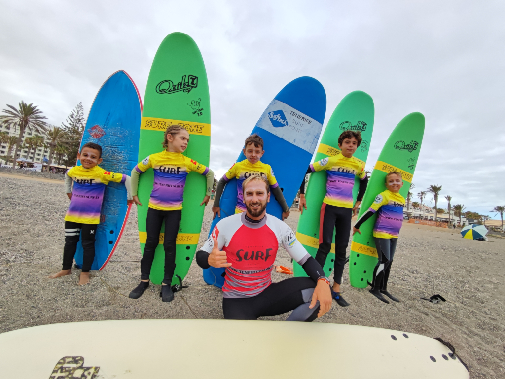 Moniteur de surf avec des enfants tenant des planches sur la plage de Tenerife.