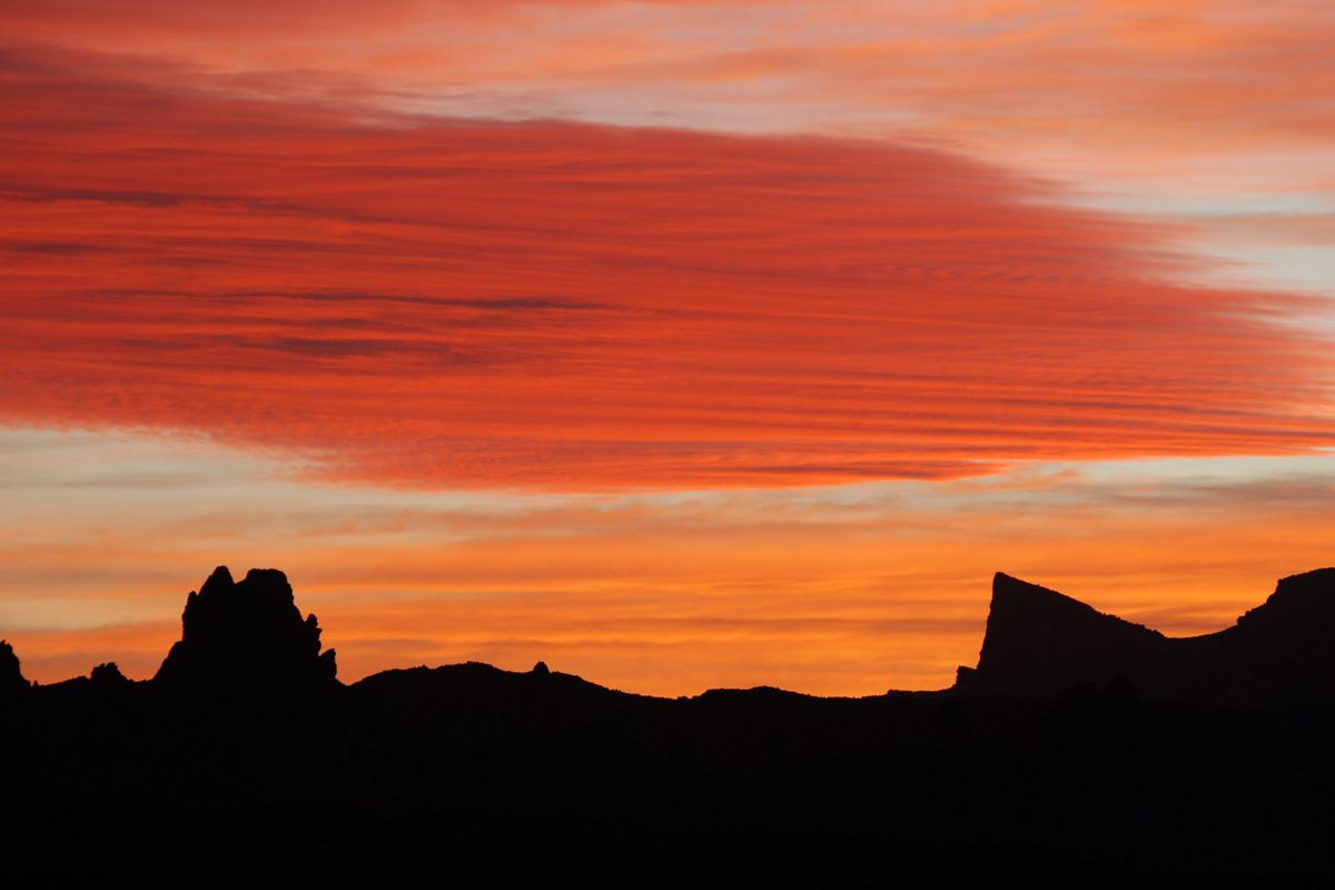 Coucher de soleil sur les montagnes de Tenerife avec des nuages rouges et un ciel orange.