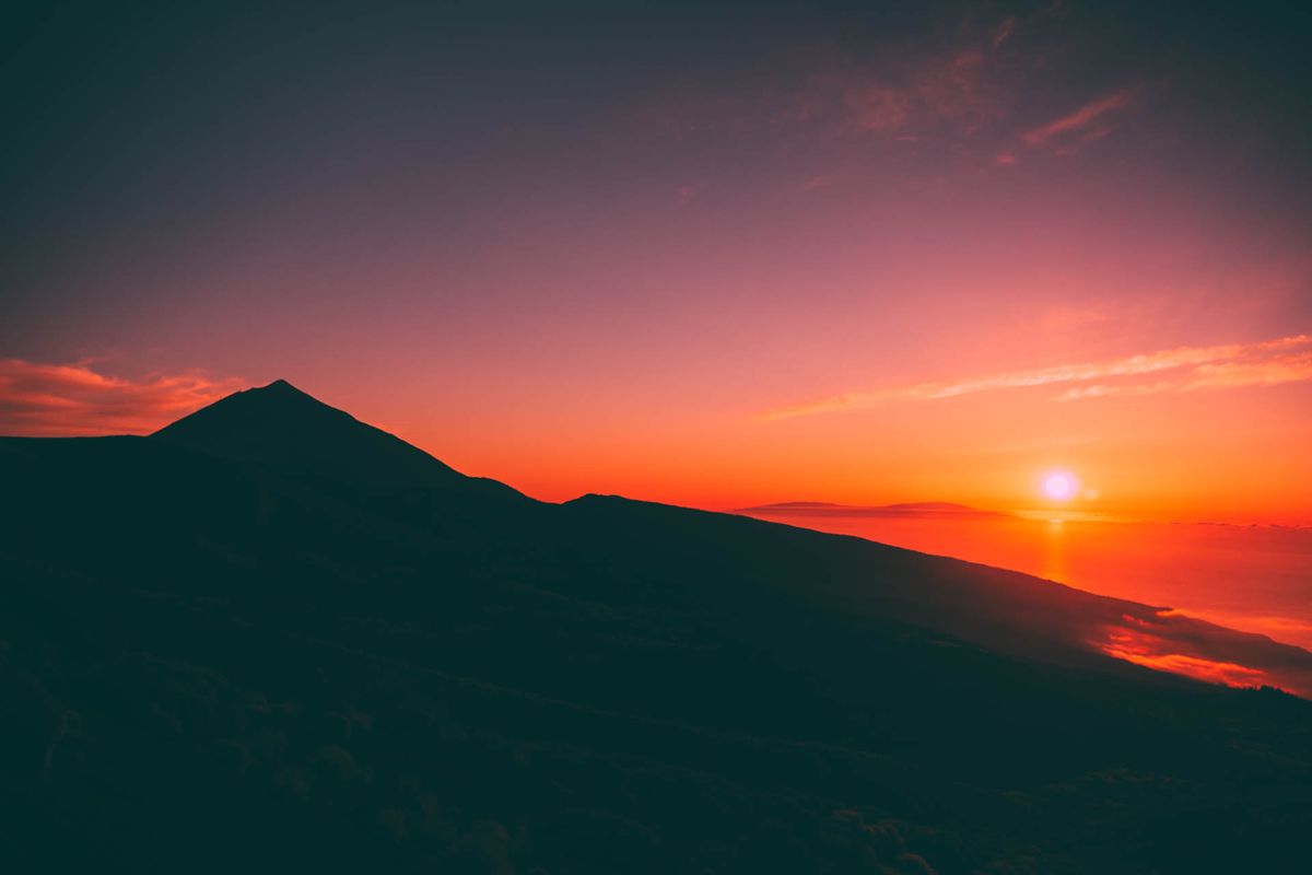Le lever du soleil au-dessus du mont Teide à Tenerife, avec un ciel rouge et un soleil à l’horizon.